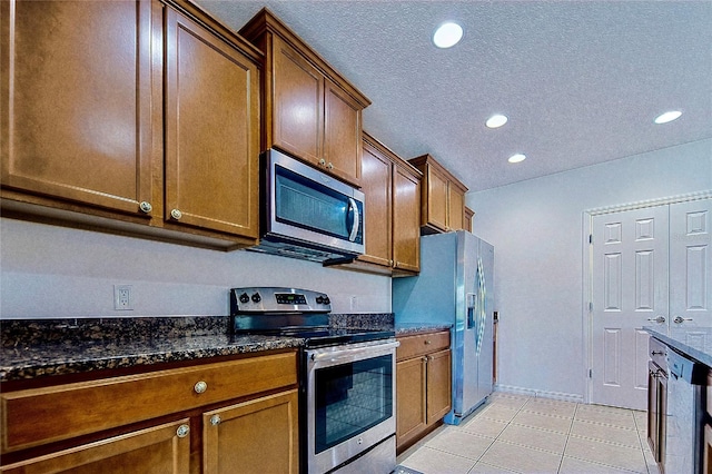 kitchen featuring dark stone counters, light tile patterned flooring, recessed lighting, appliances with stainless steel finishes, and a textured ceiling