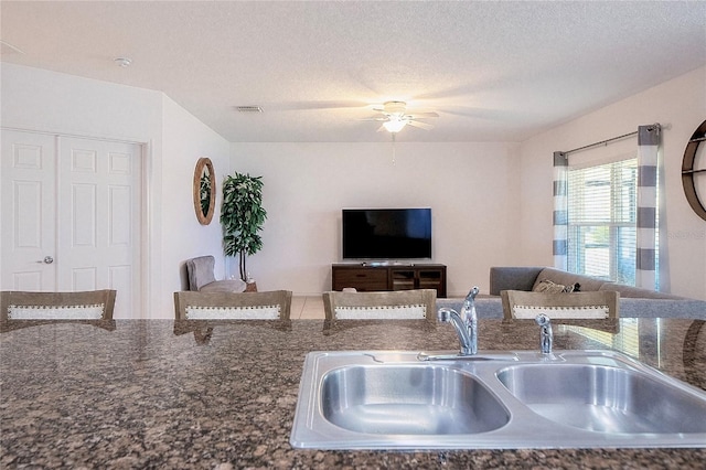 living area with visible vents, a textured ceiling, and a ceiling fan