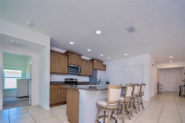 kitchen with visible vents, a breakfast bar, a center island with sink, stainless steel appliances, and light tile patterned floors