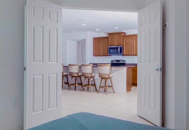 kitchen with light countertops, light tile patterned floors, recessed lighting, brown cabinets, and stainless steel appliances