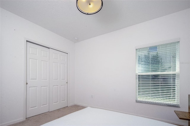 carpeted bedroom with a closet and baseboards