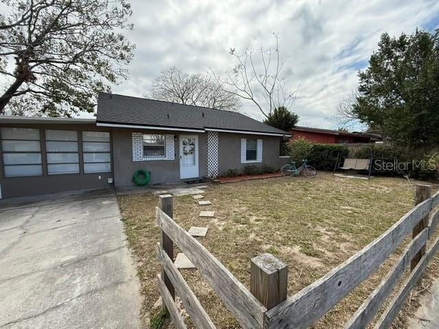 ranch-style house featuring a front yard, fence, driveway, stucco siding, and a garage