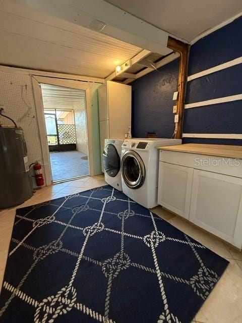 washroom featuring light tile patterned floors, cabinet space, water heater, and washer and clothes dryer