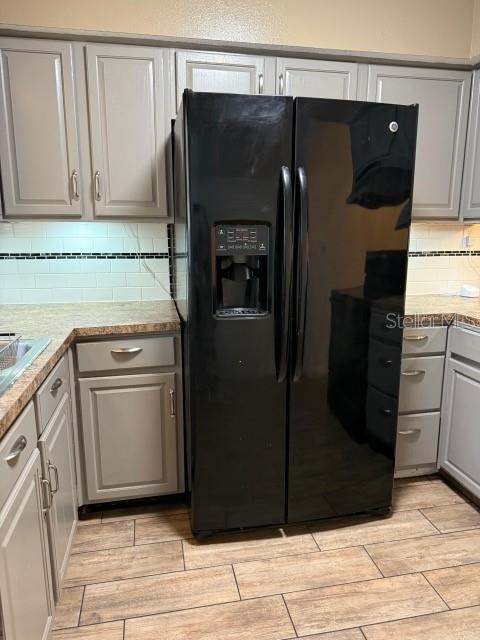 kitchen featuring gray cabinets, backsplash, black fridge with ice dispenser, light countertops, and wood tiled floor