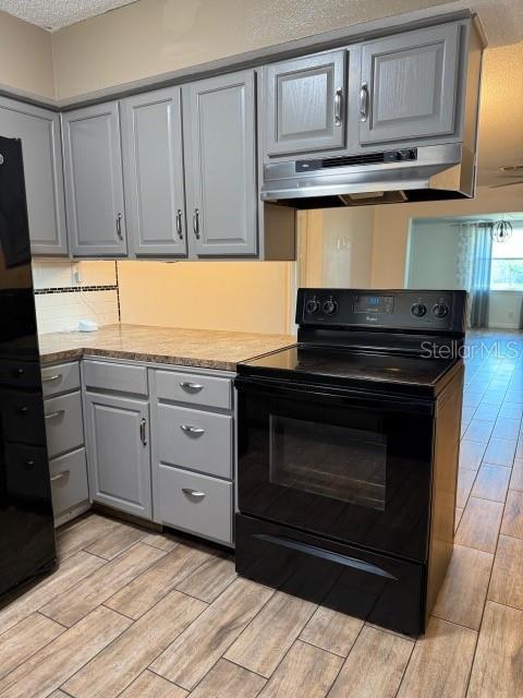 kitchen with wood finish floors, electric range, gray cabinetry, under cabinet range hood, and a textured ceiling