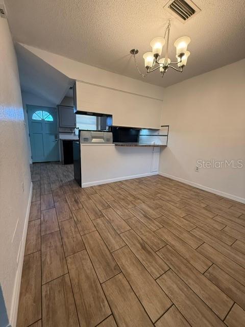 kitchen featuring visible vents, wood tiled floor, a chandelier, a peninsula, and a textured ceiling