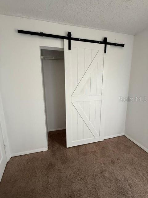 unfurnished bedroom featuring a textured ceiling, a barn door, a closet, carpet flooring, and baseboards