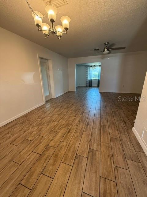 empty room featuring ceiling fan with notable chandelier, a textured ceiling, baseboards, and wood finished floors