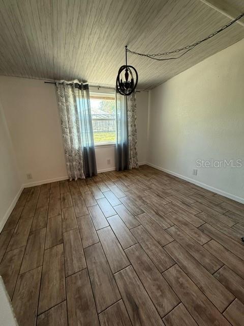 spare room featuring baseboards, wood ceiling, an inviting chandelier, and wood finished floors