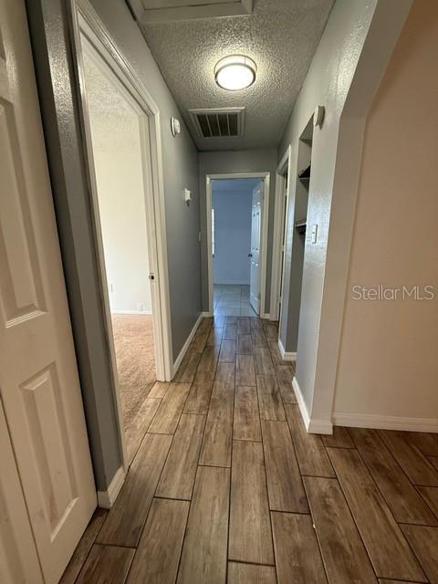 corridor with visible vents, a textured ceiling, baseboards, and wood tiled floor