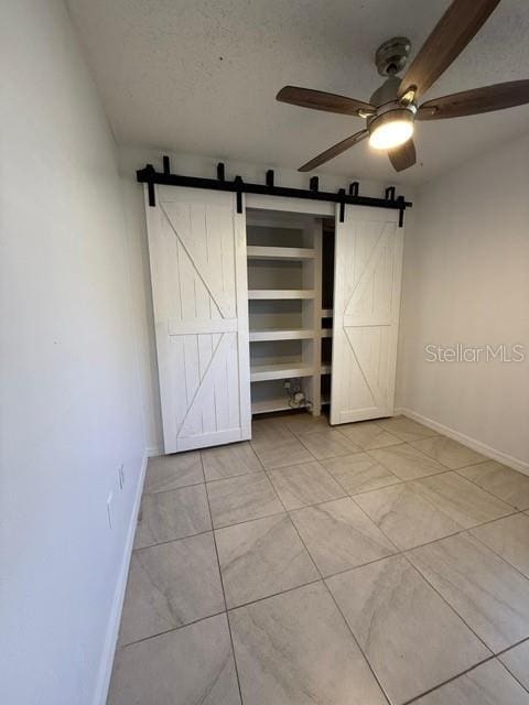 unfurnished bedroom featuring ceiling fan, a barn door, baseboards, and a textured ceiling