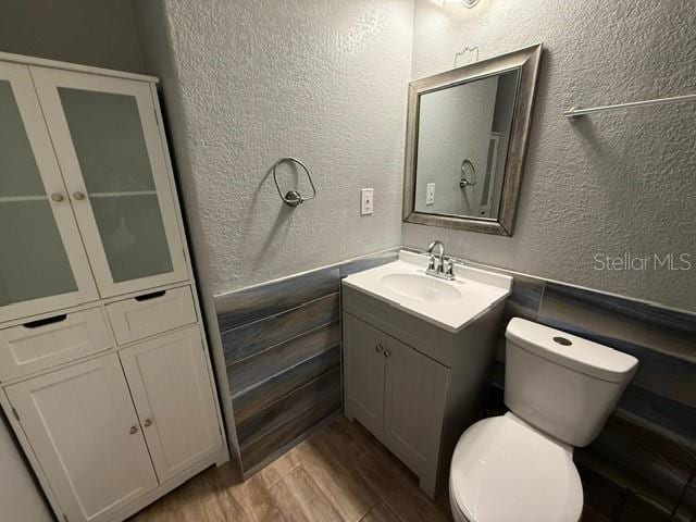 bathroom with toilet, wood finished floors, vanity, and a textured wall