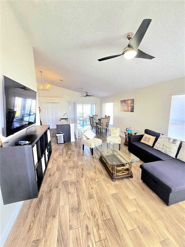 living area with light wood-style flooring, a textured ceiling, and ceiling fan with notable chandelier