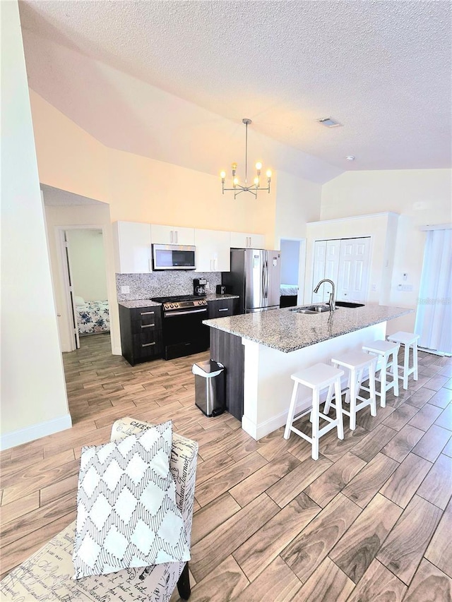 kitchen with a notable chandelier, a center island with sink, white cabinetry, appliances with stainless steel finishes, and lofted ceiling