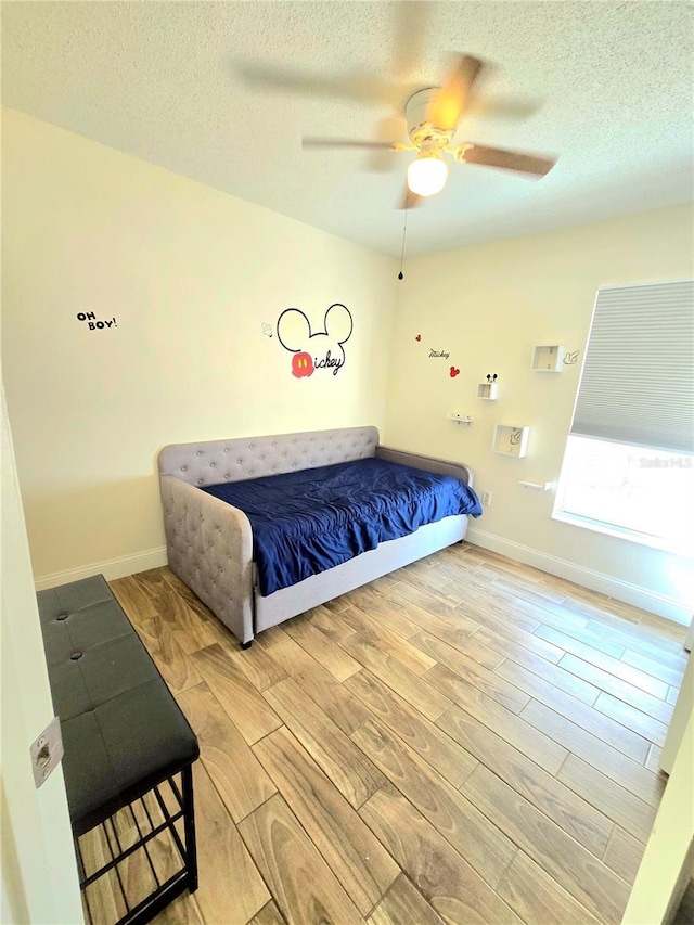 bedroom featuring a ceiling fan, wood finished floors, baseboards, and a textured ceiling