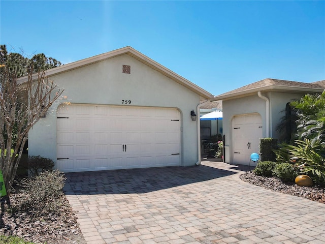 view of front facade with stucco siding, decorative driveway, and a garage