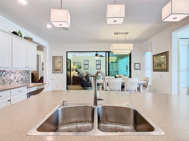 kitchen featuring a sink, decorative light fixtures, backsplash, white cabinets, and light countertops