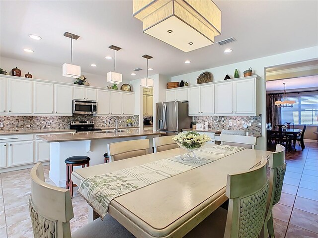 kitchen featuring light tile patterned floors, visible vents, an island with sink, stainless steel appliances, and a kitchen breakfast bar
