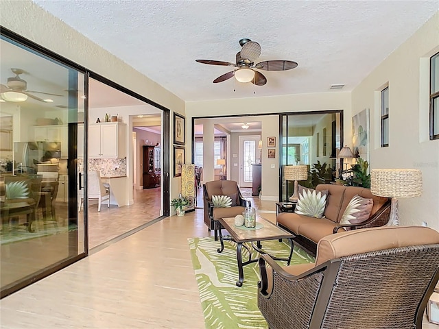 living room featuring visible vents, a textured ceiling, light wood-type flooring, and a ceiling fan