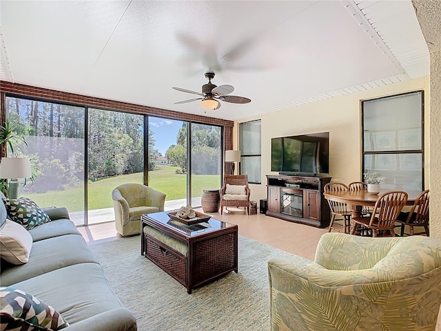 living area featuring a glass covered fireplace, expansive windows, and ceiling fan