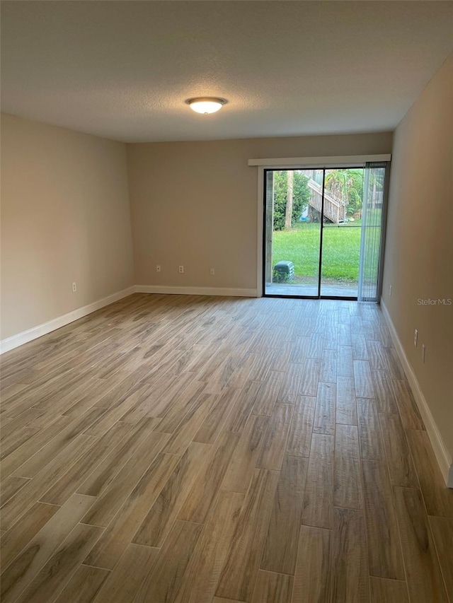 empty room featuring a textured ceiling, baseboards, and wood finished floors