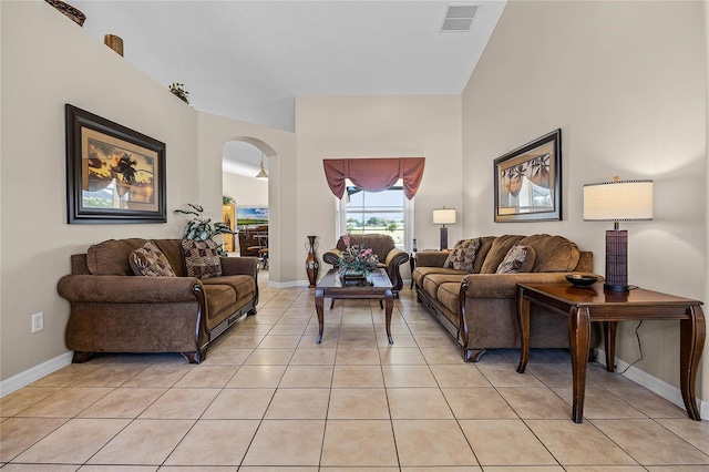 living area with light tile patterned floors, arched walkways, visible vents, and baseboards