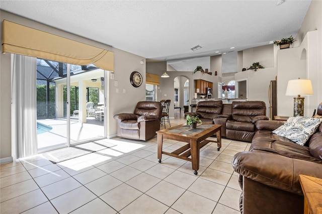 living room with visible vents, baseboards, light tile patterned floors, arched walkways, and a textured ceiling