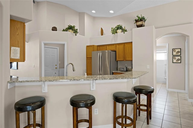 kitchen featuring a breakfast bar area, light tile patterned floors, brown cabinets, a peninsula, and freestanding refrigerator