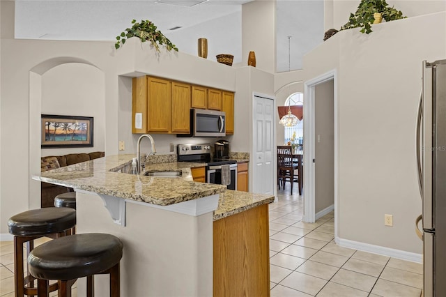 kitchen with a kitchen bar, light tile patterned floors, a peninsula, stainless steel appliances, and a sink