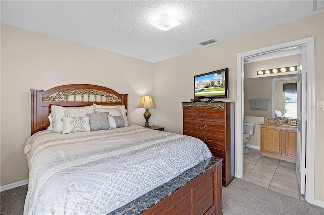 bedroom featuring visible vents, ensuite bathroom, a textured ceiling, light tile patterned flooring, and light colored carpet