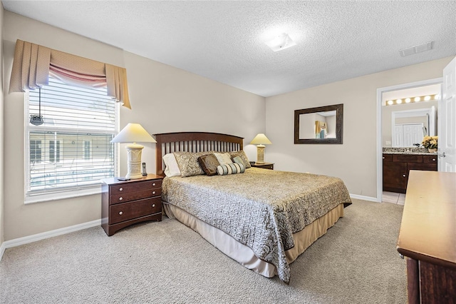 bedroom with visible vents, a textured ceiling, ensuite bath, baseboards, and light colored carpet