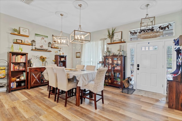 dining space with light wood-type flooring, visible vents, and an inviting chandelier