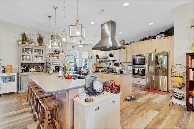 kitchen featuring island exhaust hood, light countertops, a large island, appliances with stainless steel finishes, and light wood-type flooring