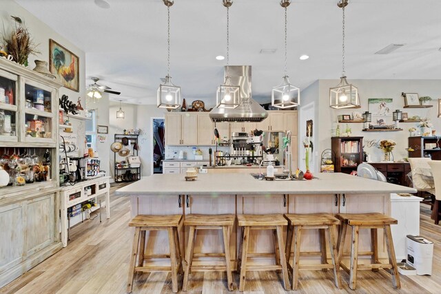 kitchen with a breakfast bar area, visible vents, island exhaust hood, light countertops, and light wood-style floors