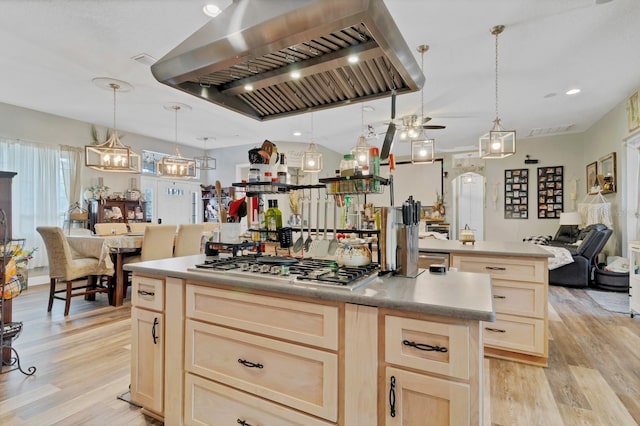 kitchen featuring light brown cabinets, a kitchen island, open floor plan, stainless steel gas stovetop, and wall chimney range hood