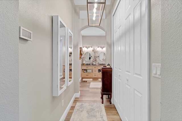 hallway with baseboards, arched walkways, light wood-style floors, and a textured wall