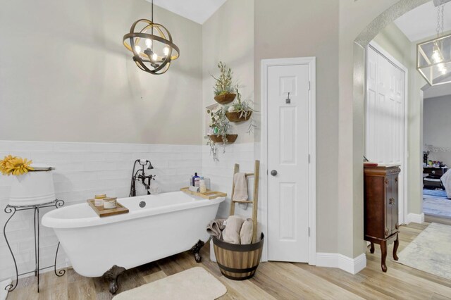 bathroom featuring a soaking tub, tile walls, wood finished floors, and wainscoting