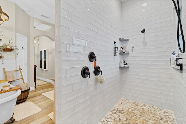 bathroom with visible vents, wood finished floors, baseboards, and tiled shower