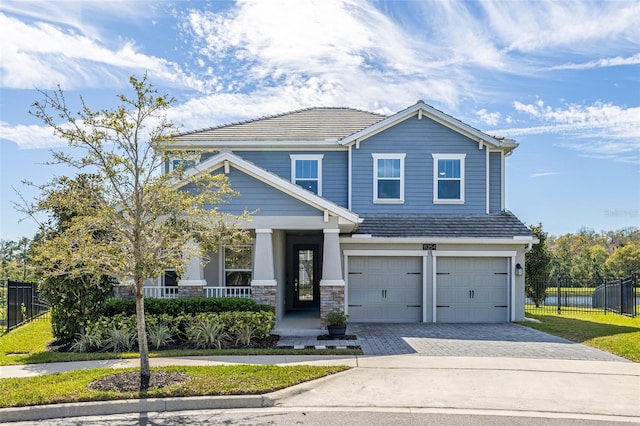 view of front of house featuring fence, a tiled roof, a porch, decorative driveway, and a garage