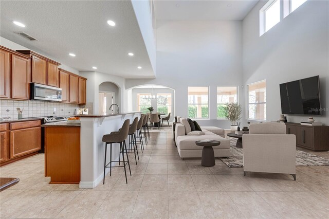 kitchen with visible vents, a breakfast bar, arched walkways, stainless steel microwave, and open floor plan