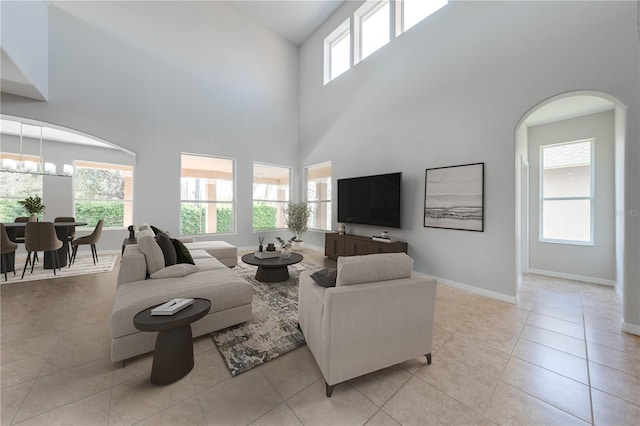 living area featuring baseboards, light tile patterned floors, a high ceiling, an inviting chandelier, and arched walkways