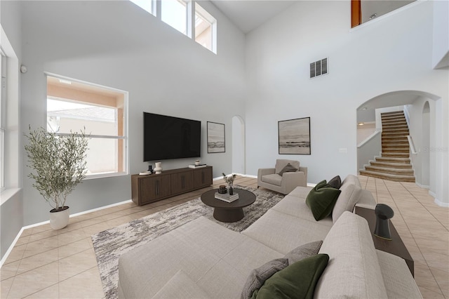 living area featuring stairway, light tile patterned floors, visible vents, and arched walkways