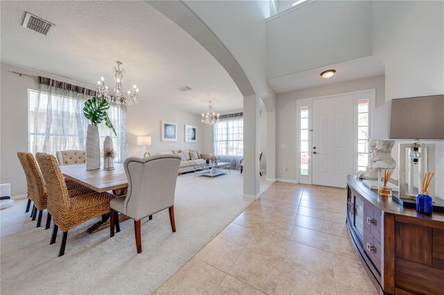 dining space with visible vents, light carpet, light tile patterned floors, an inviting chandelier, and arched walkways