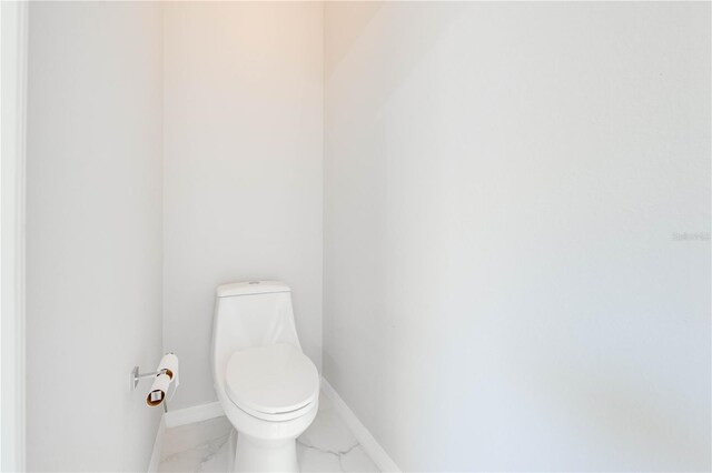 bathroom with baseboards, toilet, and marble finish floor