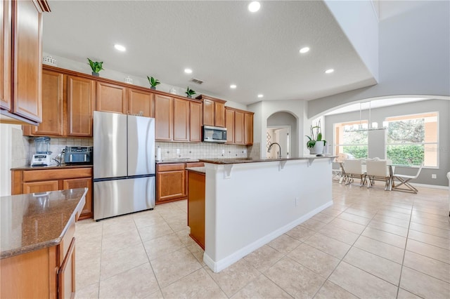 kitchen with a breakfast bar area, light tile patterned flooring, brown cabinets, and appliances with stainless steel finishes