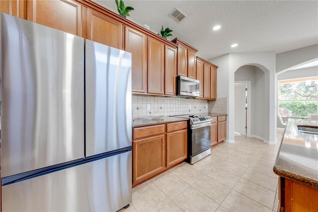 kitchen featuring tasteful backsplash, visible vents, brown cabinetry, arched walkways, and stainless steel appliances