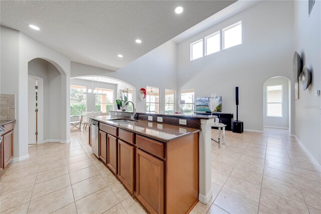 kitchen featuring dark stone countertops, brown cabinetry, arched walkways, a sink, and stainless steel dishwasher