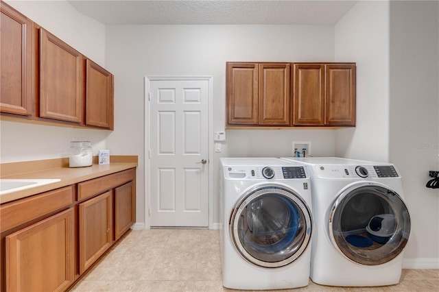 laundry area featuring baseboards, cabinet space, a textured ceiling, and washing machine and clothes dryer