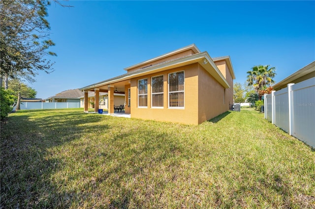 rear view of house featuring a yard, fence, and stucco siding