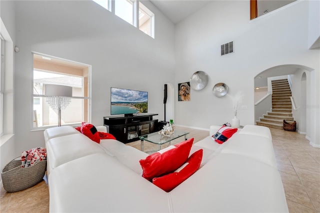 living area featuring stairway, light tile patterned floors, visible vents, arched walkways, and a towering ceiling